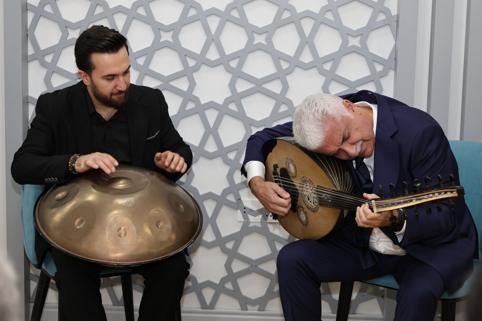 Two musicians playing oud and handpan in a cozy indoor setting, conveying cultural richness and musical harmony. — Free Spins