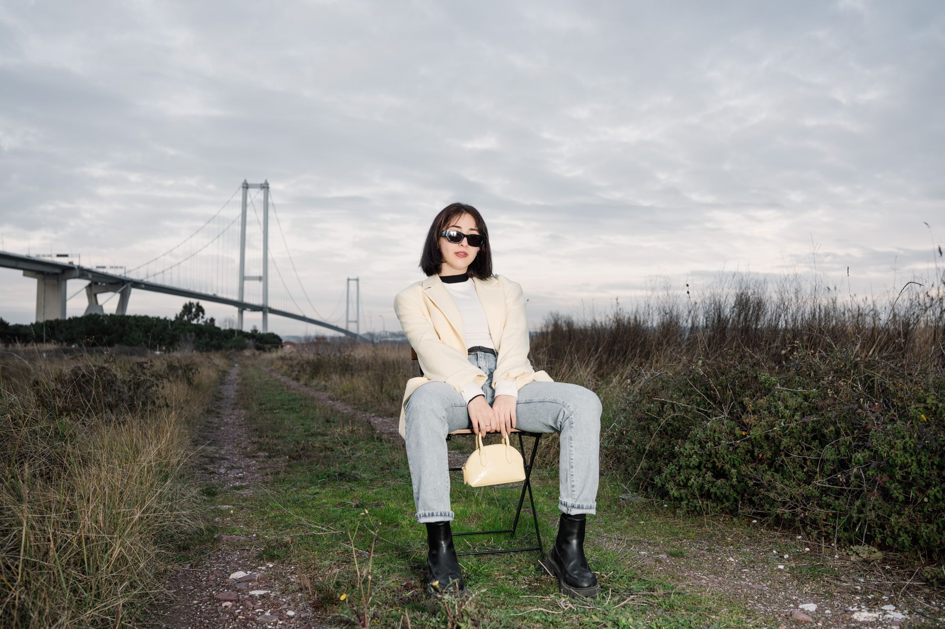 Stylish woman in sunglasses sitting by a bridge, showcasing modern fashion against a natural backdrop. — Understanding Nevada